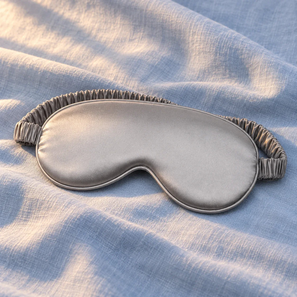 One grey satin-feel eye mask on styled blue linen